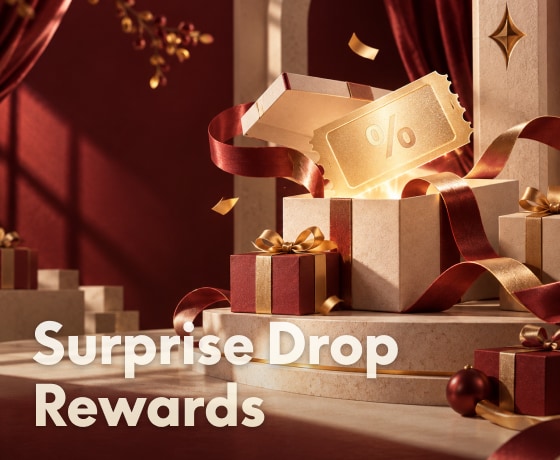 Golden ticket with percentage symbol emerging from an open gift box, surrounded by red and gold-wrapped presents on a festive stage, text reads "Surprise Drop Rewards".