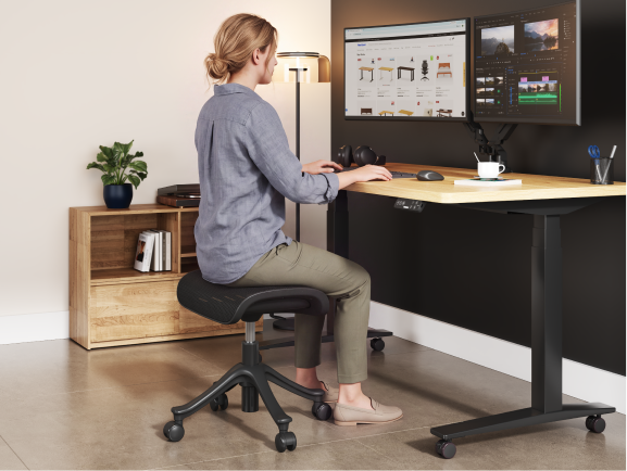 Woman sitting on the CF5 ergonomic footrest using it as an extra seat while working at a desk