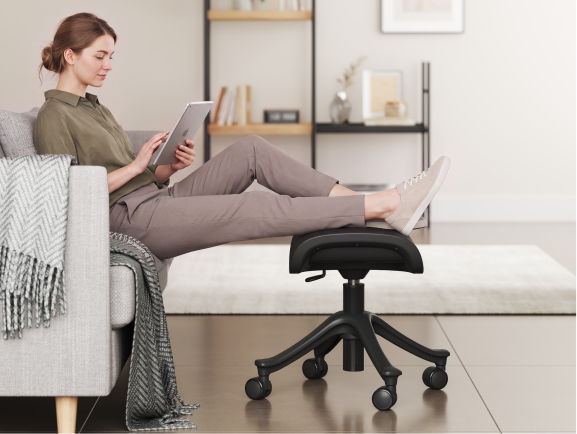 Woman relaxing on a sofa with her feet elevated on the CF5 ergonomic footrest while using a tablet