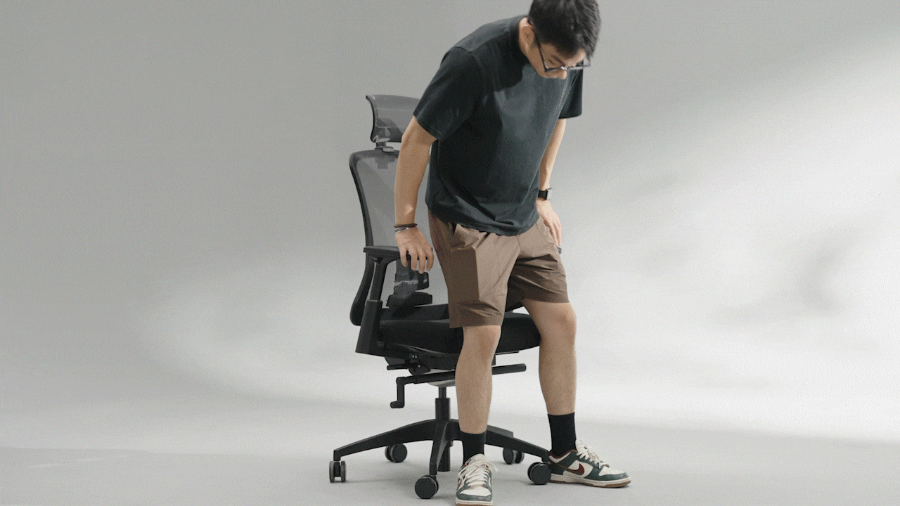 A person in casual attire adjusts a modern office chair, demonstrating its features against a neutral background.